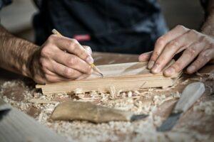Timmerman tekent met een potlood een maat af op een houten plank